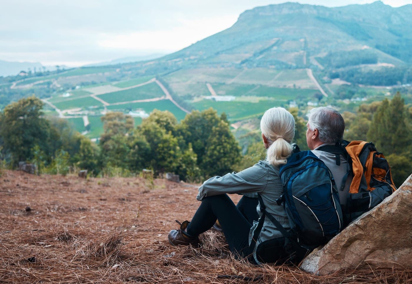 Retired couple resting on a hike while looking over a scenic mountain view.